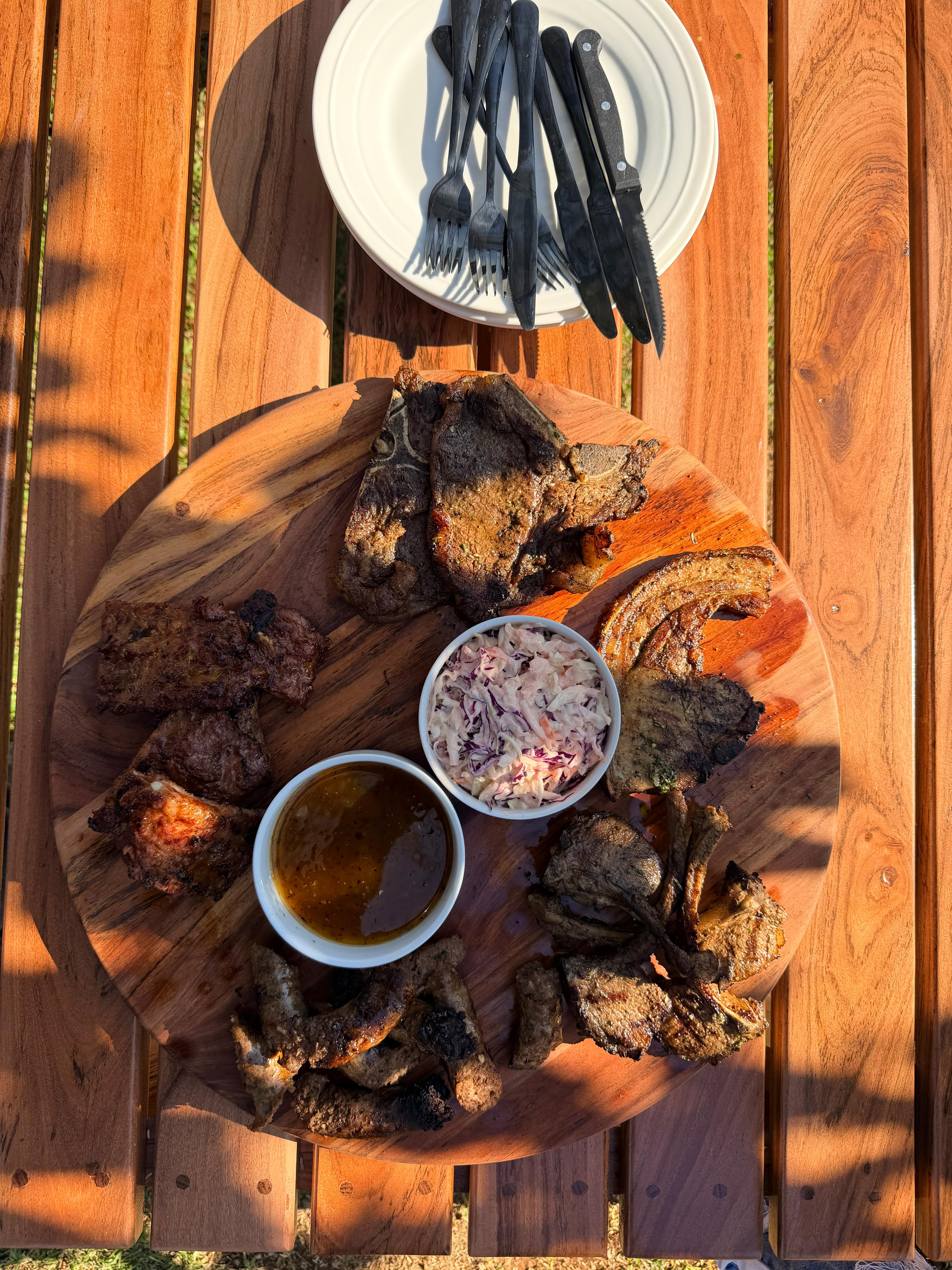 Braai platter on a round wooden board with grilled meats, coleslaw and dipping sauce