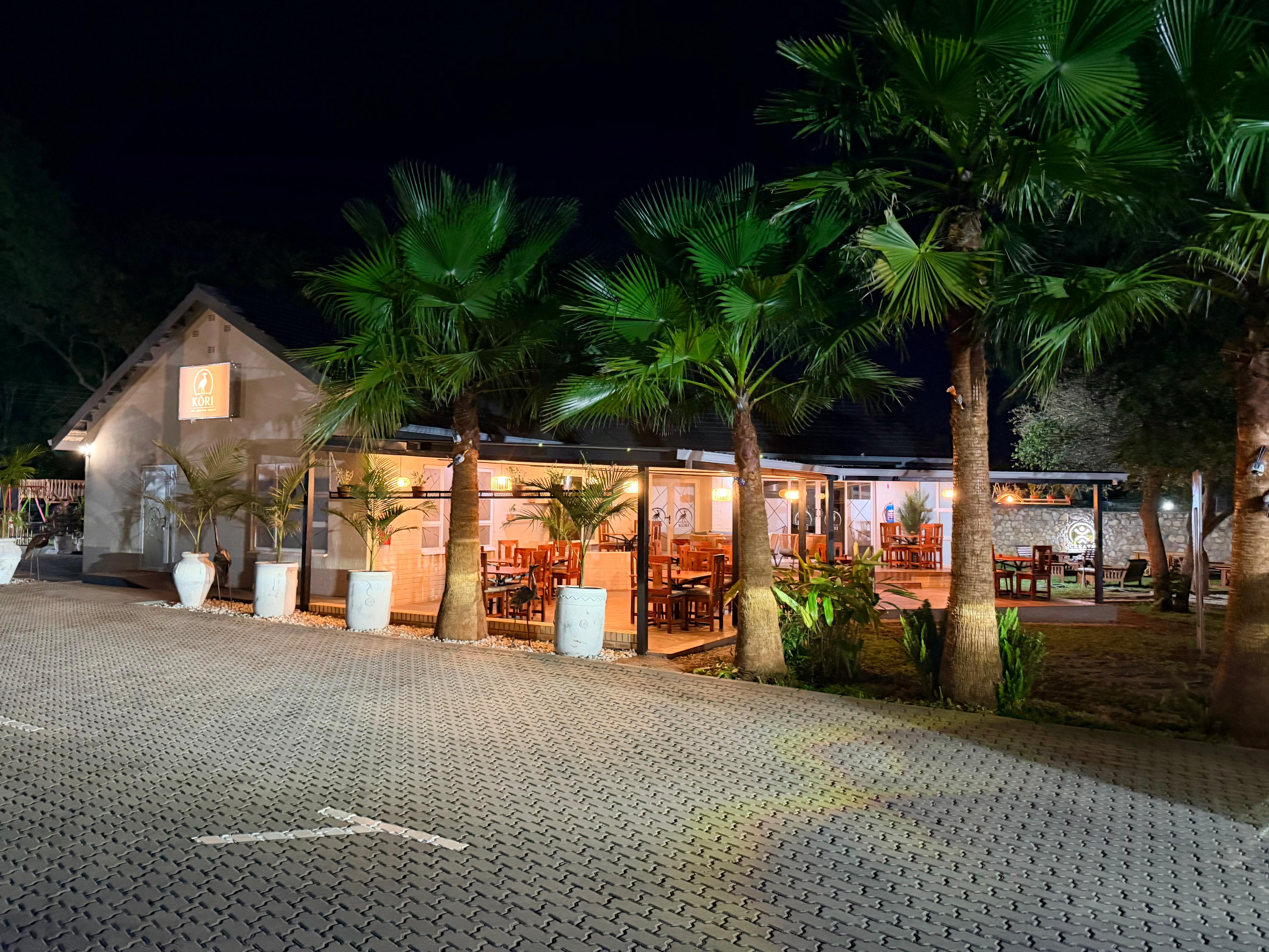 Kori Studio exterior at night — illuminated dining area with palm trees and brick driveway