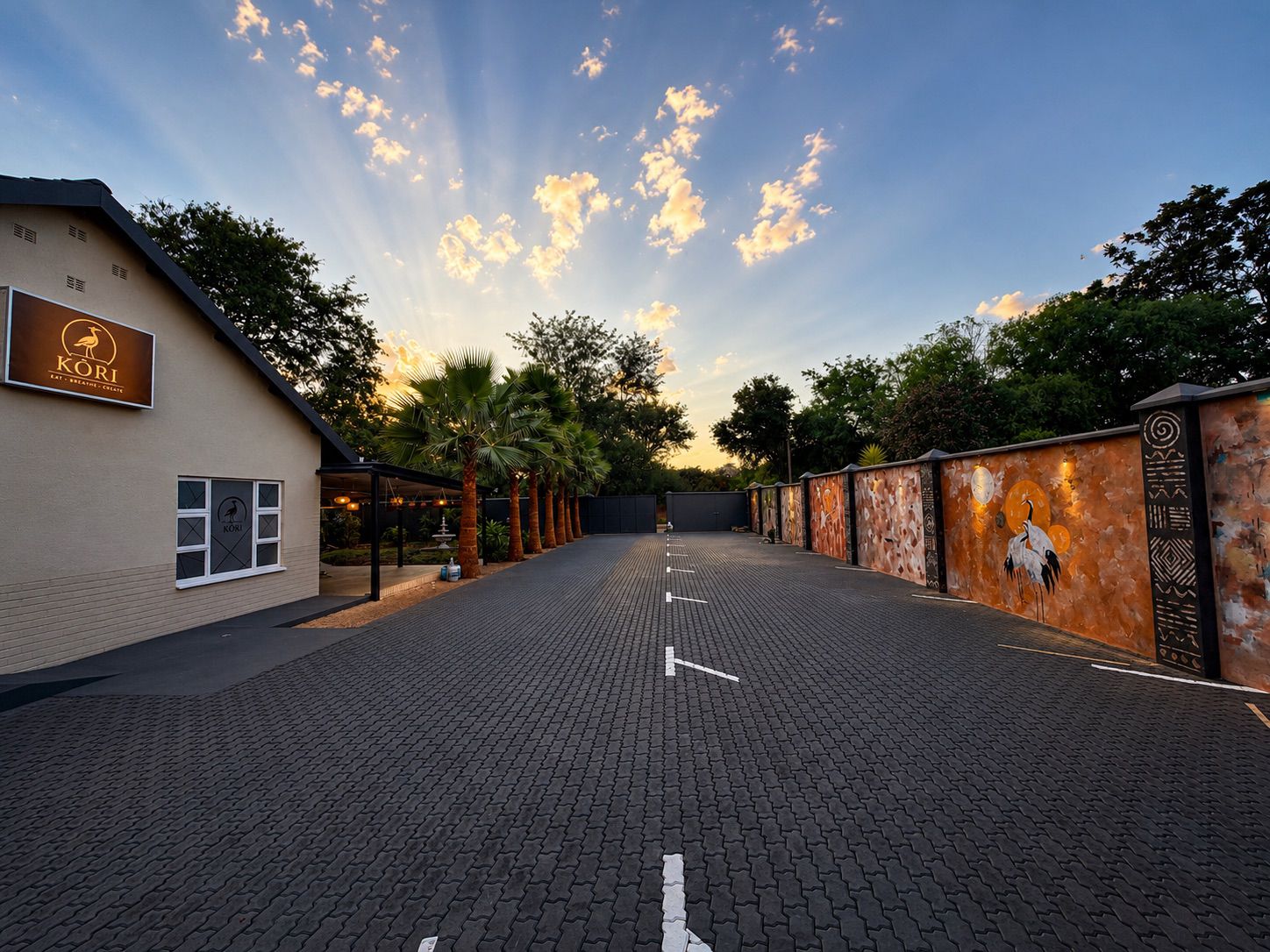 Kori Studio entrance at sunset with mural wall and palm-lined driveway
